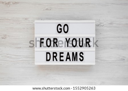 'Go for your dreams' words on a lightbox on a white wooden surface, top view. Overhead, from above, flat lay. 