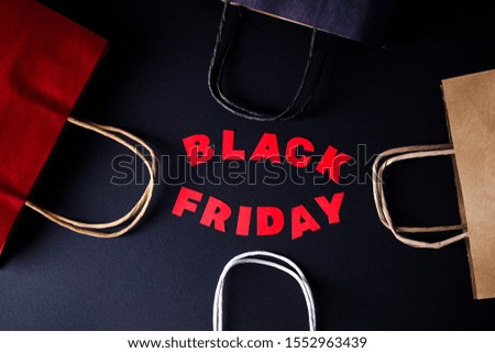 Black Friday red letters on a black background with colored kraft bags. Top view.