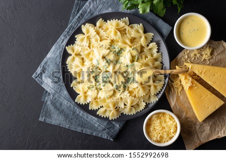 Tasty cooked italian farfalle pasta (bow-tie or butterfly) with cheese sauce. Top view. Black background. Royalty-Free Stock Photo #1552992698