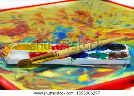 Watercolor paints of different colors with a brush on a bright surface