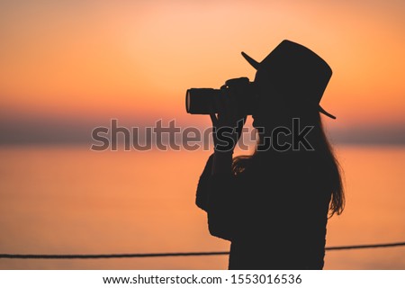 Silhouette of a woman photographer in hat with dslr camera during taking photos at sunset