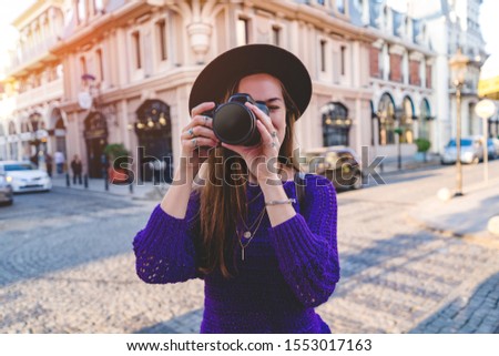 Casual stylish hipster traveler woman photographer in hat with a DSLR camera taking photos during traveling around european city