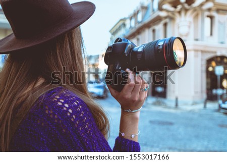 Stylish casual fashionable hipster brunette woman photographer in hat taking pictures using dslr camera and lens during walking around european city
