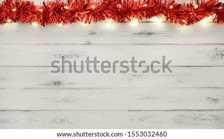 A string of red and silver christmas lights and tinsel, on a destressed white woodern background