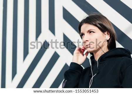 Portrait of a beautiful brunette woman in stylish clothes listening to music on a mobile device, pretty hipster girl looking at the camera.
