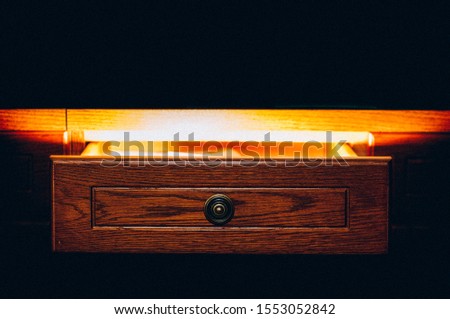 A wooden drawer immersed in a very dark environment. Intense light emerges from the inside, creating a magical effect. Royalty-Free Stock Photo #1553052842