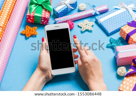Top view of phone in female hand on festive blue background. Christmas decorations. New Year time holiday. Mockup.