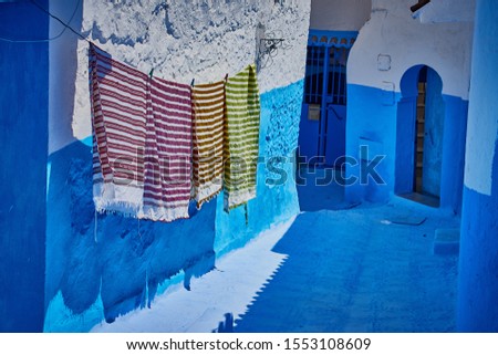 Four striped colorful towels hanging on laundry rope by blue and white wall, with two blue doors on background, shot in Chefchaouen, Morocco on sunny day