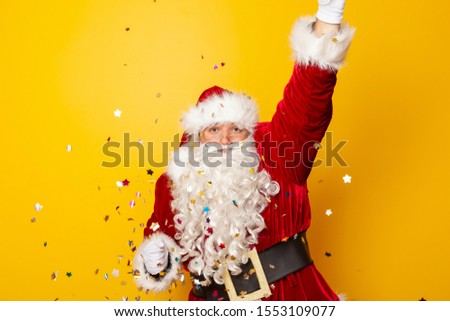 Santa Claus celebrating New Year, dancing and having fun, isolated on yellow colored background with colorful confetti all around
