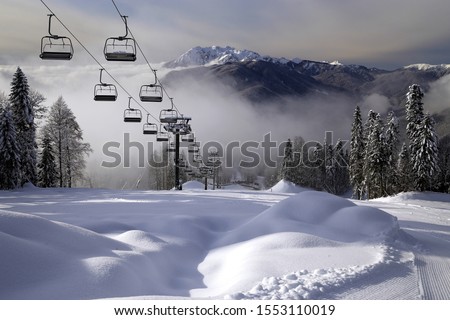 Chair ski lift in Krasnaya Polyana, Sochi, Russia on Chugush mountain peak background in Caucasus Mountains at snowy winter. Ski tracks of Gazprom ski resort on sunny day. Scenic landscape