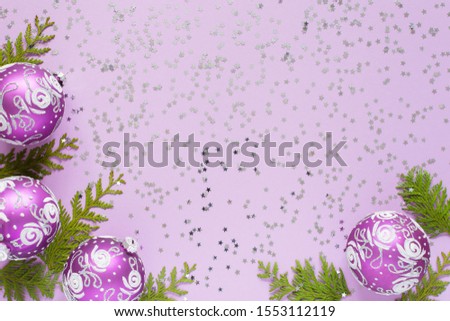 Holiday background , christmas balls and thuja twigs on a lilac background with glitter silver stars, flat lay, top view