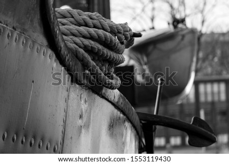 Black and white picture of a close up view of an old fishing boat, its rope, anchor and lifeboat in the background, Stockholm - 2019