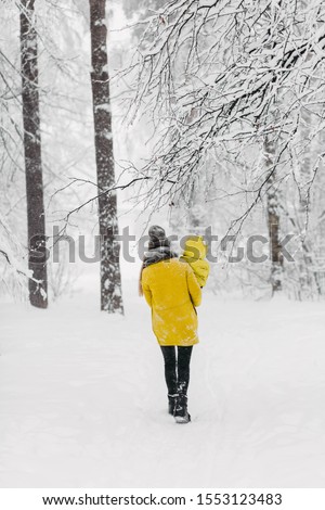 A beautiful family walks through the winter snowy forest. Mother and son in yellow jackets enjoying day outdoors. Holidays, christmas, happiness together, childhood in love.