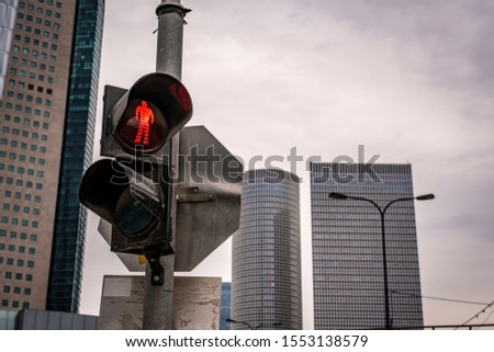 Traffic light for pedestrians with a red signal in the shape of a man. City buildings in the background.