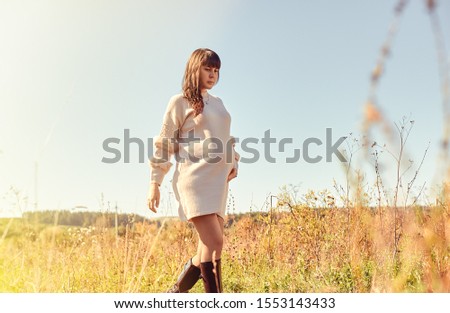 Image of a young pregnant girl takes a walk in sunny weather, holds her tummy with one hand.