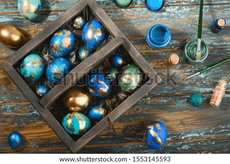 Painted colored Easter eggs in dark wooden box on dark wooden background. Boho stile.