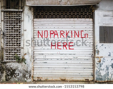 A No Parking sign painted in the color red on the white, shuttered door of a shop on a street in Thakur Village in the suburb of Kandivali East in the city of Mumbai.