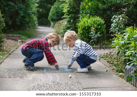 Two little sibling boys painting with chalk outdoors in summer