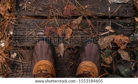 boots on a wooden walkway surrounded by fall leaves.
