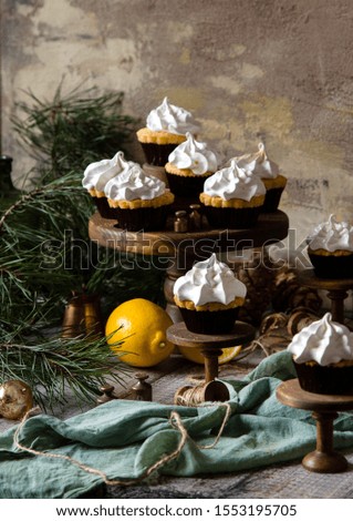 homemade lemon cupcakes with whipped meringue on wooden cake stands on grey table with fir tree branches. christmas sweets