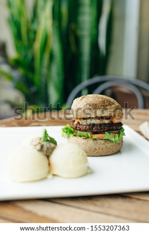 Vegan big bean burger with mashed potato in classic bun, served on white plate. 