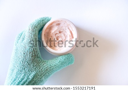 Hand in green exfoliating glove holding pink strawberry scrub or mask on light background. Skin care beauty concept.