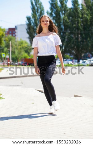 Full body young model. Portrait of young beautiful brunette woman in jeans and white blouse walking in summer street