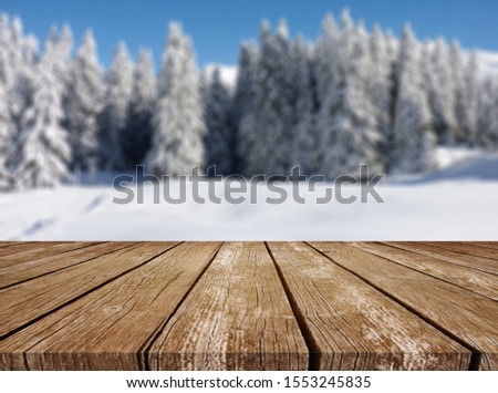 Wooden table top on winter sunny landscape with fir trees. Merry Christmas and happy New Year greeting background. Winter landscape with snow and christmas trees.