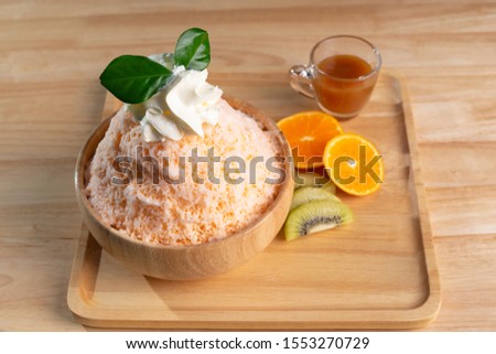 Bingsu or shaved ice in a wooden cup decorated with oranges and kiwi