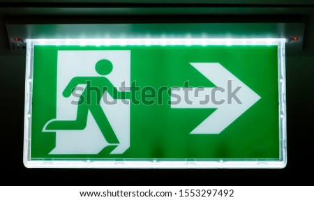 Generic green exit safety sign for building evacuation in case of an emergency. Graphic of a human figure walking through a door with a white arrow indicating the path.
