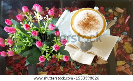 
Hot Cappuccino Coffee Placed on a table with a beautiful design, decorated with dried flowers that emit a light, fragrant aroma, served with sugar The side of the coffee mug has a coffee spoon placed