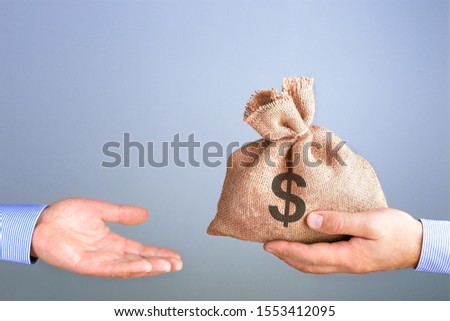 Man holds, gives a bag of money in hand like a bonus. Businessman holding bag of money in hand offering bribe with copy space. Cash bag concept. Royalty-Free Stock Photo #1553412095