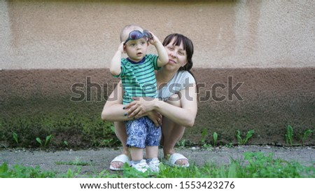 Funny baby and his squating mom hugging him. Child holds glasses over his head