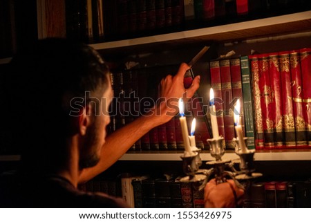 Boy holding book from the library in the dark with candles to light his way