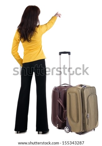 Young traveling woman with  suitcas points at wall. The rear view .