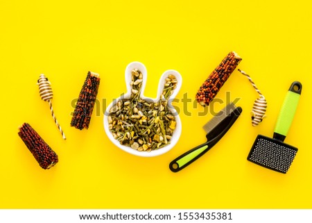 Pet care. Dry food for home rodents like rabbit and hamsters near accessories on yellow background top view copy space