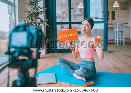 Blogger doing giveaway. Cheerful famous fitness blogger wearing short top doing giveaway in her blog Royalty-Free Stock Photo #1553467580