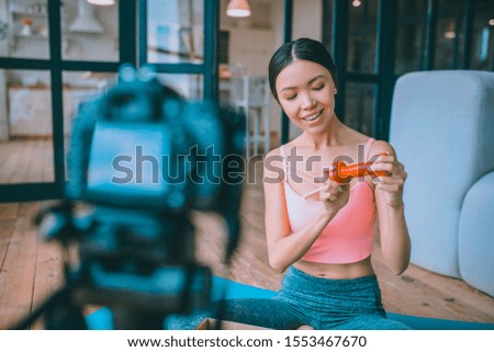 Blogger showing barbell. Smiling slim fitness blogger showing barbell while making video