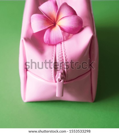 Pink cosmetic bag and Hawaiian plumeria tropical flower on vivid green background. Beauty concept.