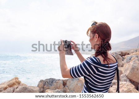 Attractive mature traveler woman use mobile phone take a photo of beautiful seascape. Copy space.