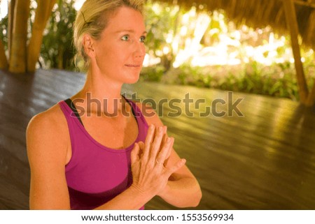 young happy and beautiful blond American woman doing yoga workout in Bali at exotic bamboo hut opened to forest view sitting in namaste hands pose meditating enjoying retreat in harmony