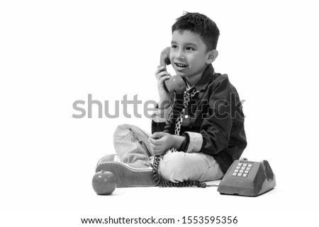 Studio shot of cute happy boy smiling and talking on old telephone while thinking