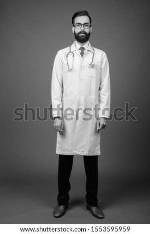 Young handsome bearded Persian man doctor against gray background