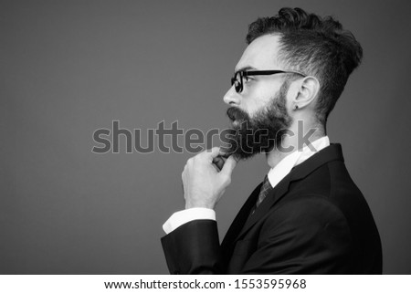 Young handsome bearded Persian businessman against gray background