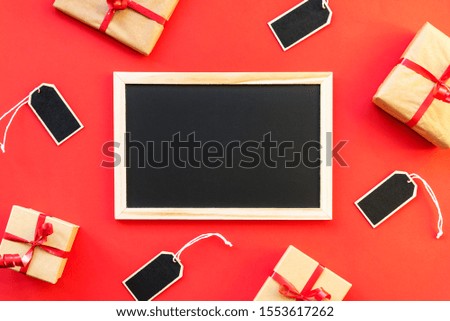 Black chalk board on a red background surrounded by gifts and price labels, Holiday shopping on black friday concept, mock up.