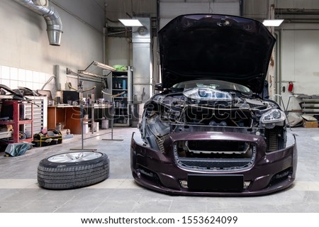 The brown car in the body of the sedan is preparing for painting the body without headlights and bumper in a workshop for repair vehicles. Auto service industry. Royalty-Free Stock Photo #1553624099