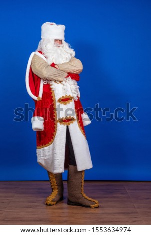 Emotional Santa Claus with a long white beard in a red coat and white hat posing on a blue background