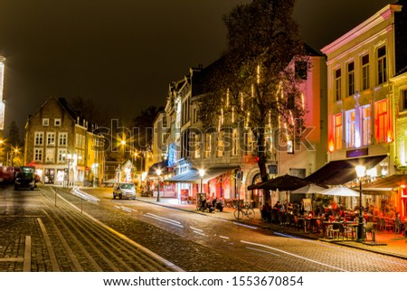 Cityscape of a quiet evening of a cobbled street, buildings, restaurant terraces, parked cars and different colored lighting in the city of Maastricht, South Limburg, The Netherlands