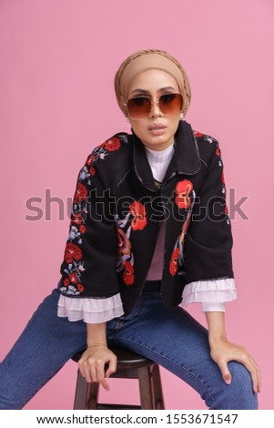 Fashionable beautiful model in jeans, long sleeves floral jacket and hijab isolated on pink background. Stylish Muslim hijab fashion lifestyle portraiture concept.