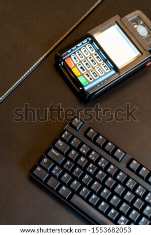 Picture of Modern payment terminal and credit cards on black background with computer keyboard, top view.
